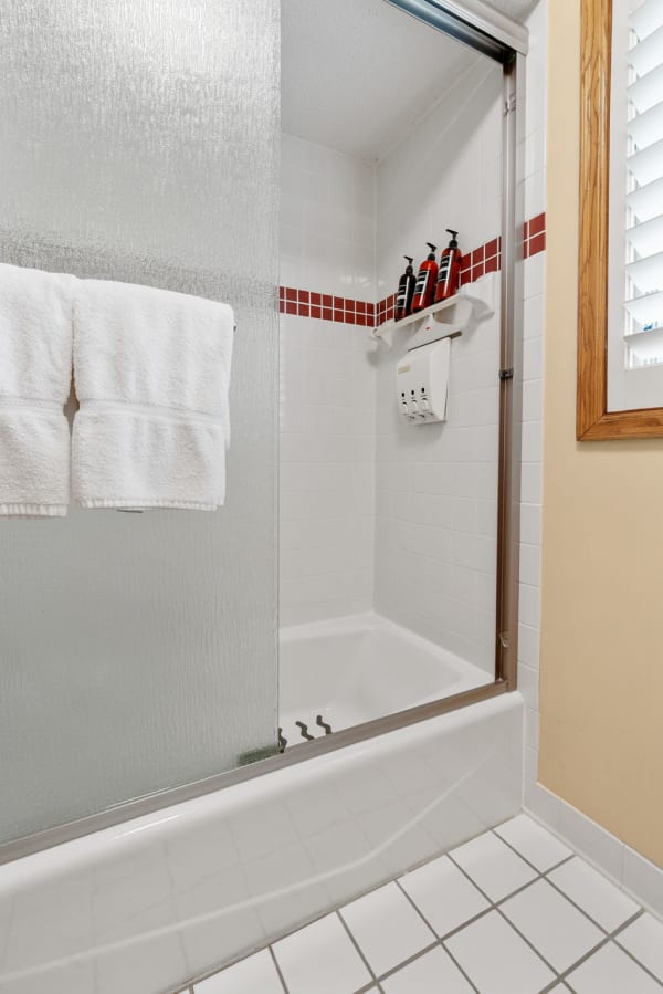 A modern shower with frosted glass and neatly arranged toiletries against white tiles.