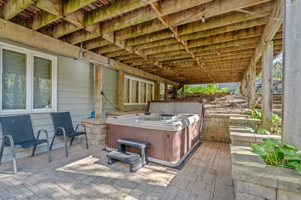 Hot tub and patio chairs under a wooden deck in a backyard space.