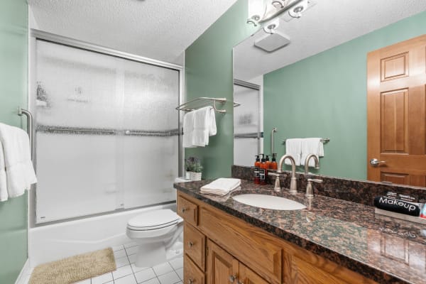 A modern bathroom with a green wall, glass shower, and granite countertop.