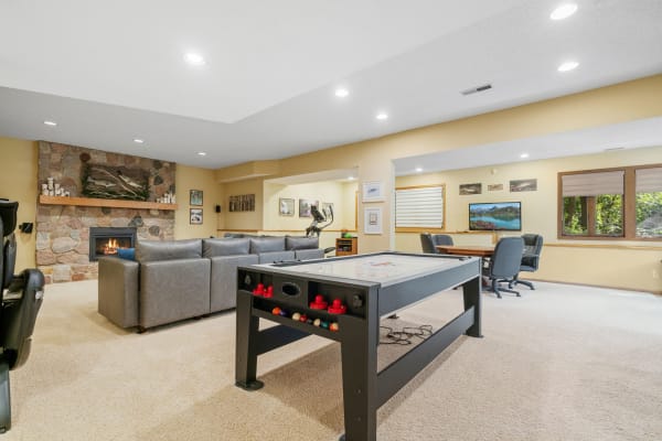 Spacious basement with air hockey table, gray sofa, and stone fireplace.