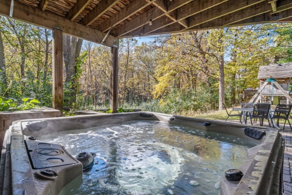 Hot tub beneath a gazebo, surrounded by trees with autumn leaves, and outdoor seating area.