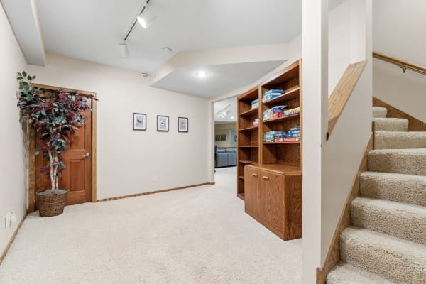 A well-lit basement entry with stairs, a decorative plant, and a shelving unit filled with games.