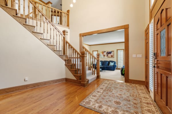 An entryway with a wooden staircase, hardwood floor, and view of a living room behind a doorway.