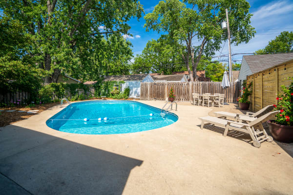 A clear swimming pool surrounded by concrete and seating under a blue sky.