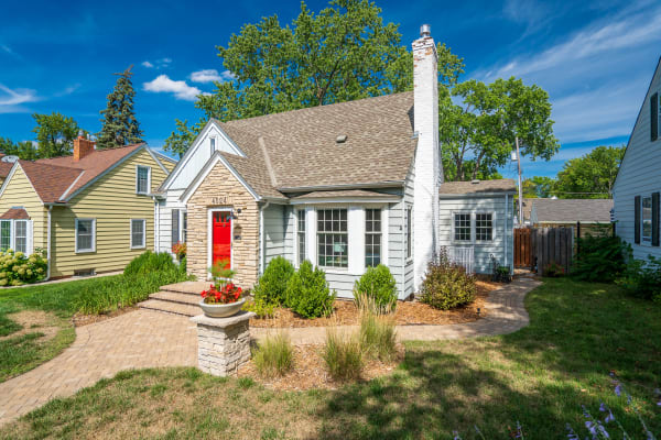 Front view of a single-story house with a red door, surrounded by greenery and colorful flowers.