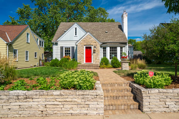 A two-story home with a red front door, blue siding, and stone accents, surrounded by green lawns and flower beds.