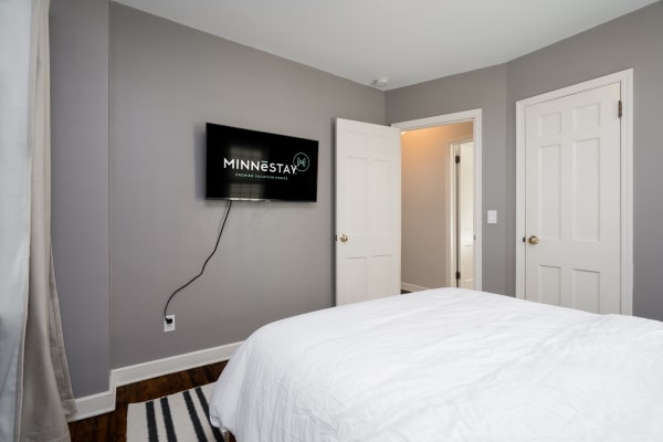 A contemporary bedroom with a white bedspread, mounted TV, and gray walls.