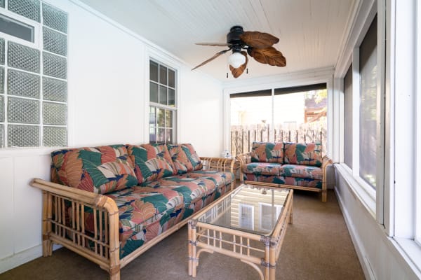 Bright sunroom featuring bamboo-framed sofas with tropical leaf upholstery, a glass coffee table, and a ceiling fan.
