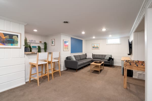 A modern basement living area featuring a gray sectional sofa, bar area, and foosball table.