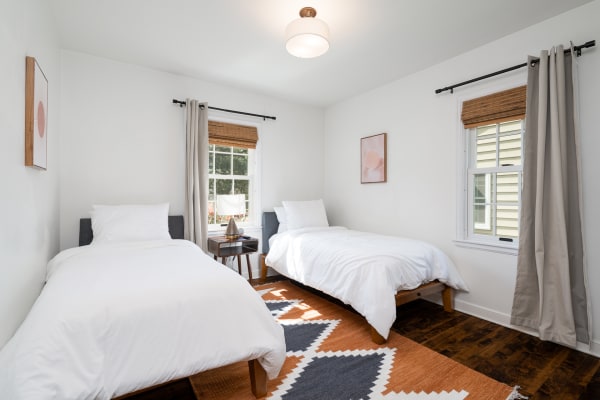 A twin bedroom with two beds, a wooden nightstand, a lamp, and an abstract art piece on the wall.
