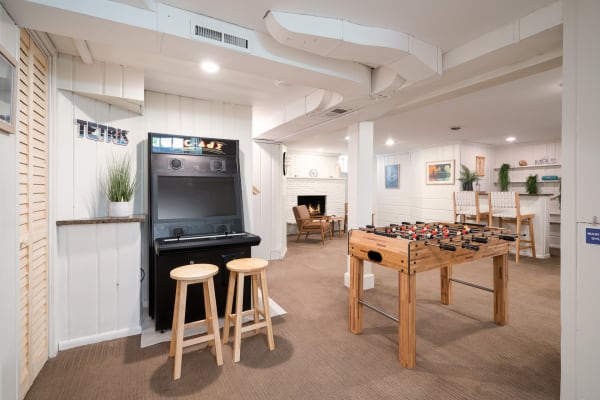 A comfortable game room featuring an arcade game, foosball table, and cozy seating area.