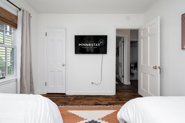 A cozy bedroom with two beds, a flat-screen TV displaying MINNESTAY, and a view to a bathroom.