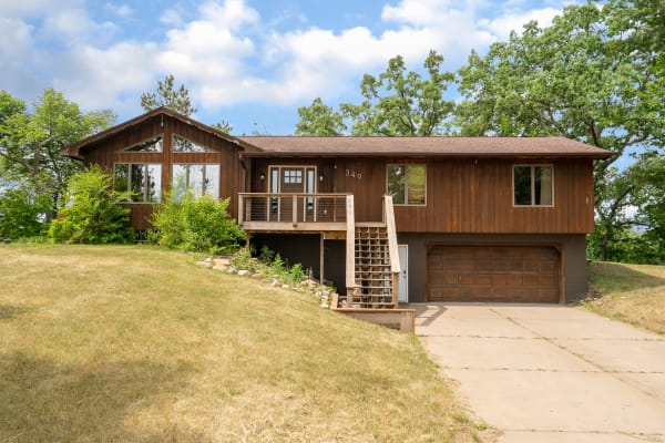 A split-level house with a wooden facade, large windows, and a welcoming deck, surrounded by greenery and a blue sky.