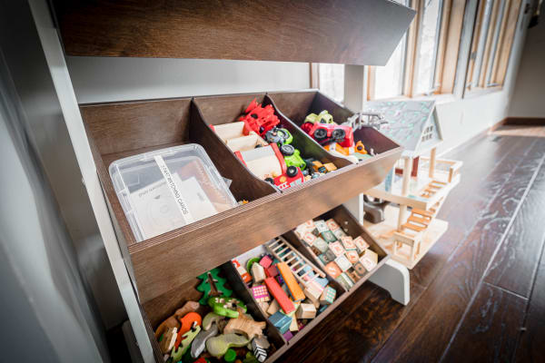 Toy storage unit with various colorful toys and a small wooden house model.
