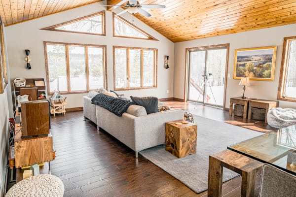 Cozy living room with a gray sofa, wooden furniture, and large windows showing a snowy landscape.