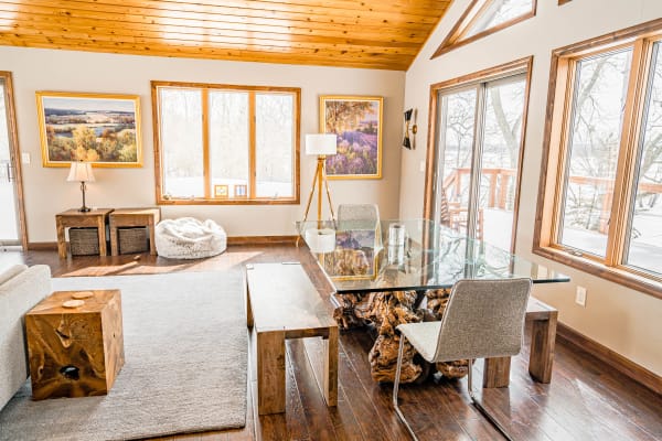 A bright living room featuring wooden beams, large windows, and a glass dining table.