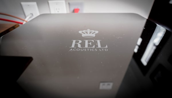 Close-up of REL Acoustics Ltd device with logo and electrical outlets in the background.