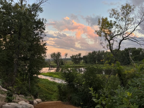 A riverbank scene at sunset with colorful clouds and trees.