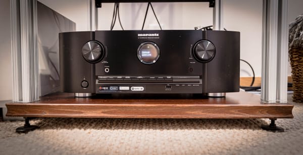 A black Marantz AV surround receiver with a digital display and knobs, placed on a wooden surface.