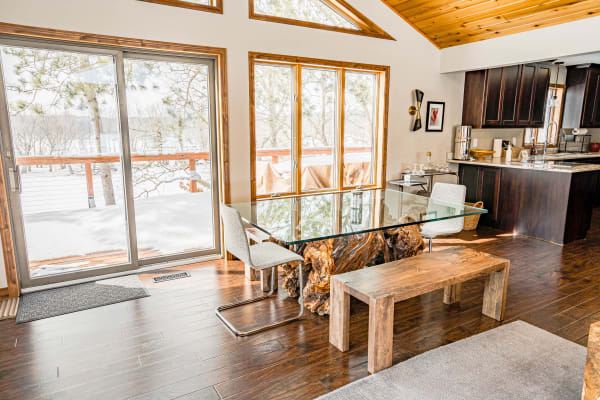 A contemporary dining area with a glass table, wood accents, and large windows showing a snowy landscape.