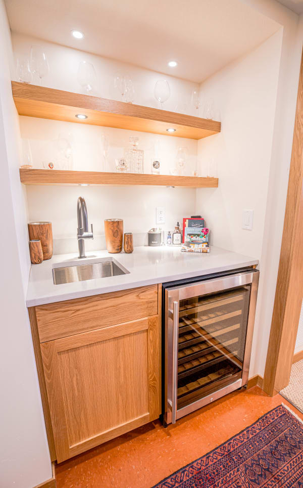 A stylish home bar area featuring a sink, wine cooler, and wooden shelves with glasses.