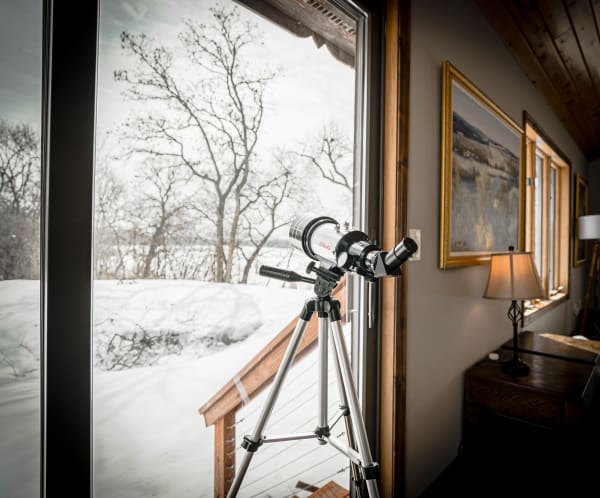 A telescope set up by a window overlooking a snowy landscape.