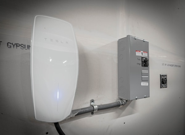 A Tesla wall charger and an electrical sub-panel on a textured wall.