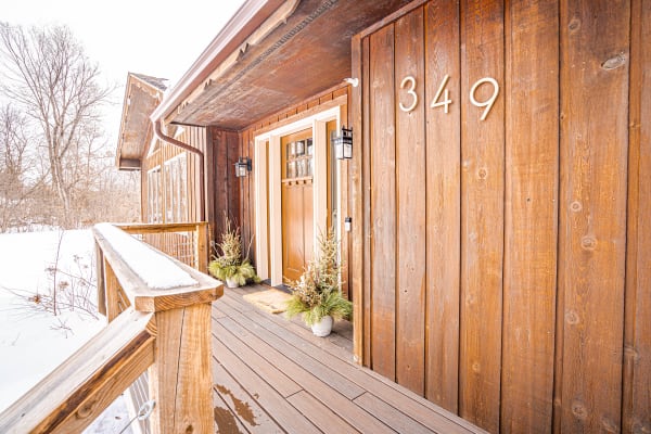 Entrance of a wooden house with snow, featuring a brown door and potted plants.