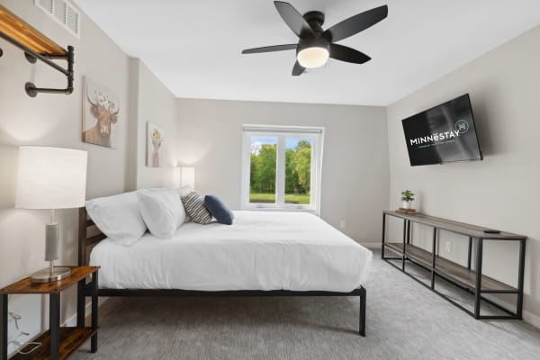 Serene and modern bedroom featuring a bed with white linens, decorative pillows, and a large window overlooking greenery.