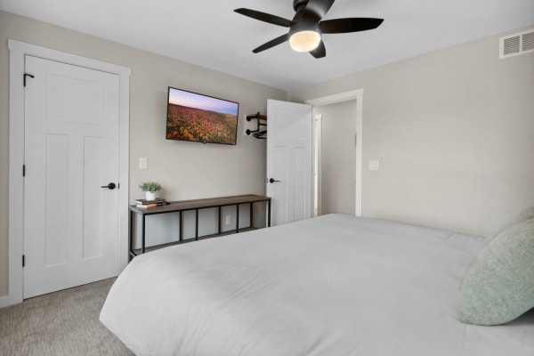 Minimalist modern bedroom with white bedding, wall-mounted TV, and stylish decor.
