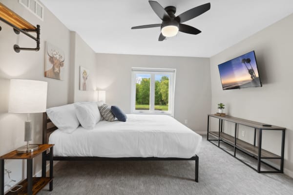 Modern bedroom with white bed linens, decorative pillows, animal artwork, and a view of greenery outside.