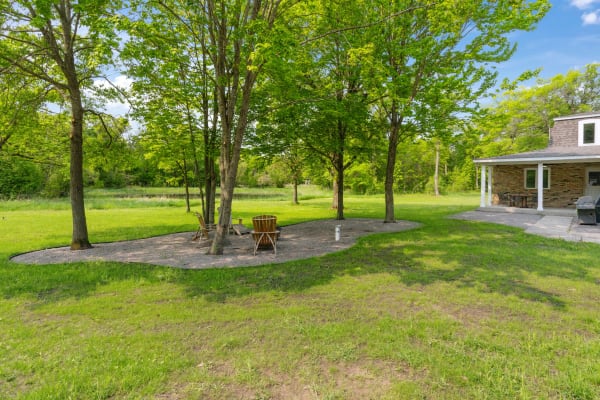 Outdoor seating area with chairs under trees in a lush green landscape.