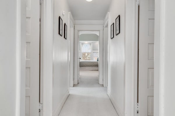 A long white hallway with framed pictures and closed doors, leading to a bedroom.