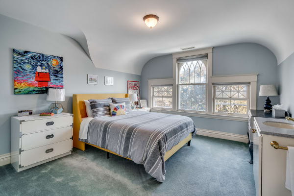 A stylish bedroom featuring a yellow bed, gray striped blanket, and vibrant artwork on the wall.