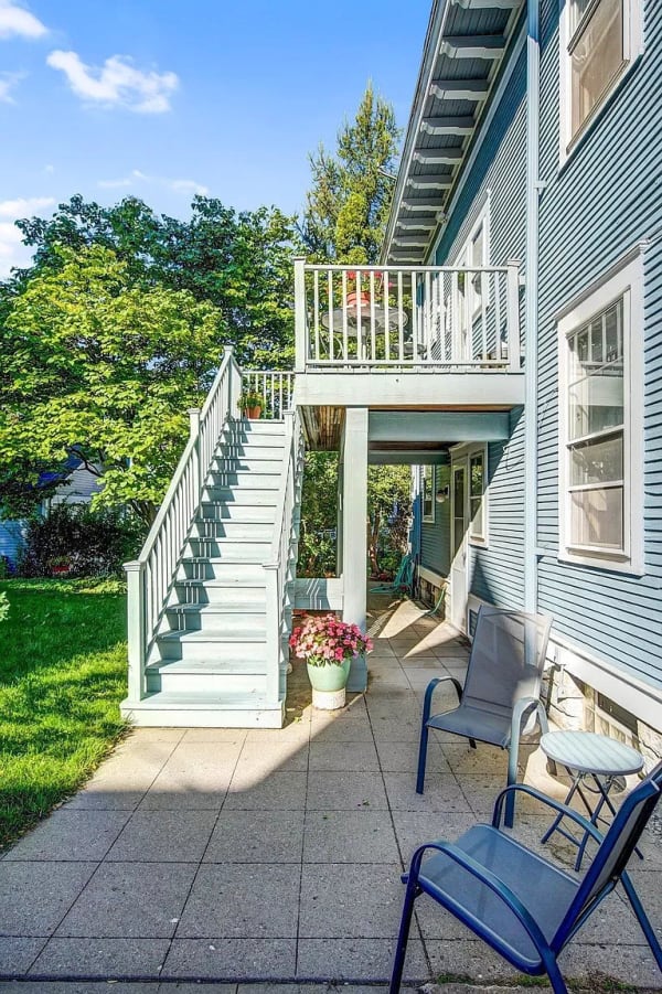 Wooden staircase leading to a porch of a blue house, surrounded by green grass and flowers.