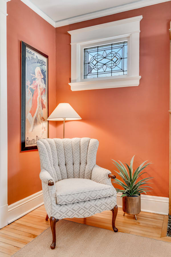 A cozy corner of a room with a plush armchair, lamp, and decorative plant against a coral wall.