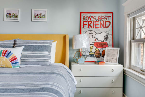 A stylish bedroom with a yellow headboard, striped bedding, and decorative lamp; colorful cartoon art hangs on the wall.