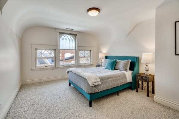 A bright bedroom with a turquoise bed, gray bedding, and warm lighting from bedside lamps.