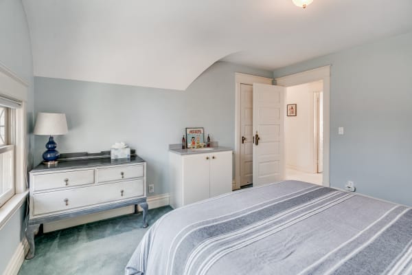 A cozy bedroom with a bed, blue walls, a vintage dresser, and soft carpet.