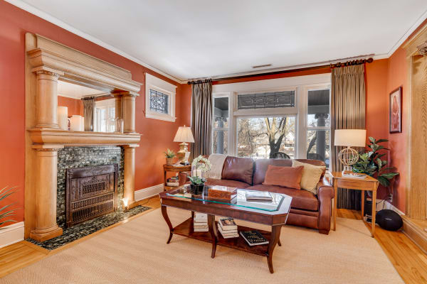 A warm terracotta living room featuring a wooden fireplace, leather sofa, and large windows.