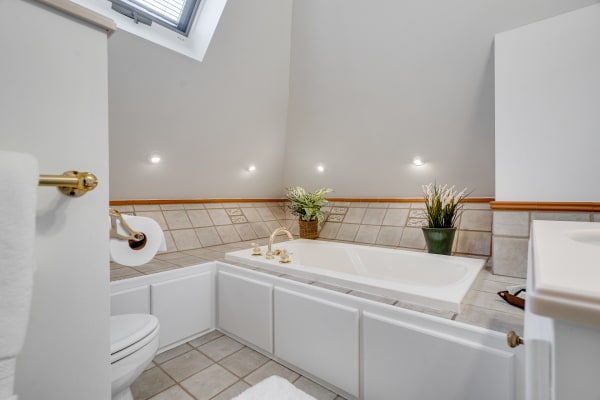 Modern bathroom with a bathtub, nature-inspired decor, and soft lighting under a sloped ceiling.