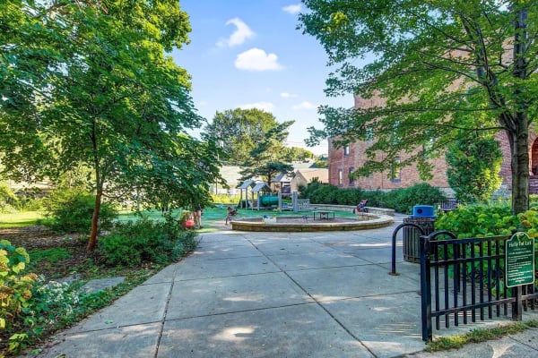 A park featuring a circular play area, lush trees, and a brick building in the background.