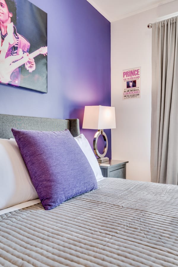 Cozy bedroom with purple walls, a portrait of a musician, and grey bedding.