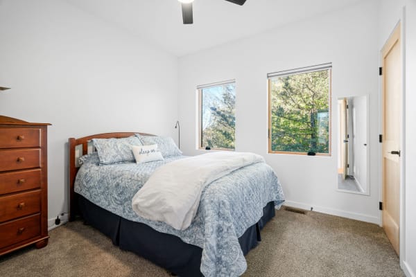 Cozy bedroom with wooden bed, blue patterned bedding, and large windows bringing in natural light.
