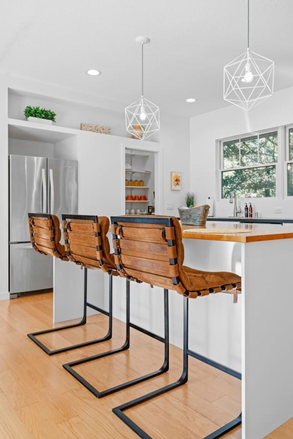 Modern kitchen with brown leather bar stools and geometric pendant lights.
