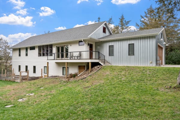 Modern two-story house with a mix of white siding and gray metal, featuring a balcony and large windows.