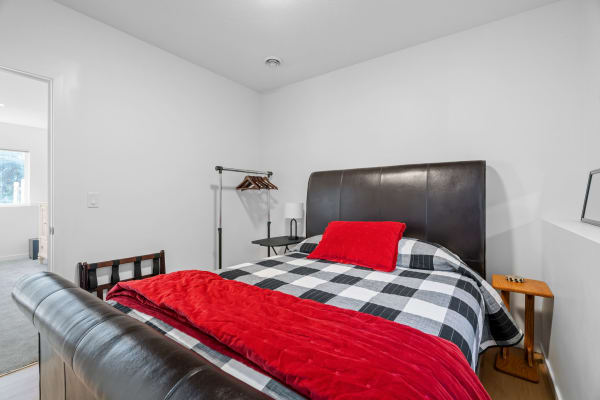 A modern bedroom featuring a bed with a leather headboard, checkered bedding, and a bright red throw blanket.