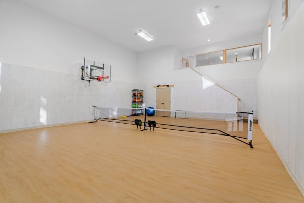 Indoor gym featuring a basketball hoop, exercise equipment, and a badminton court setup.