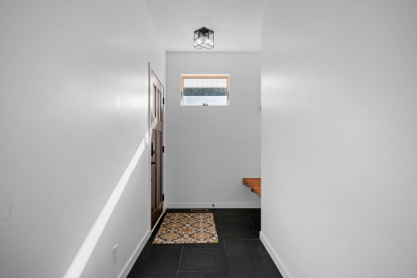 A minimalist hallway featuring a wooden door, patterned doormat, and geometric light fixture.