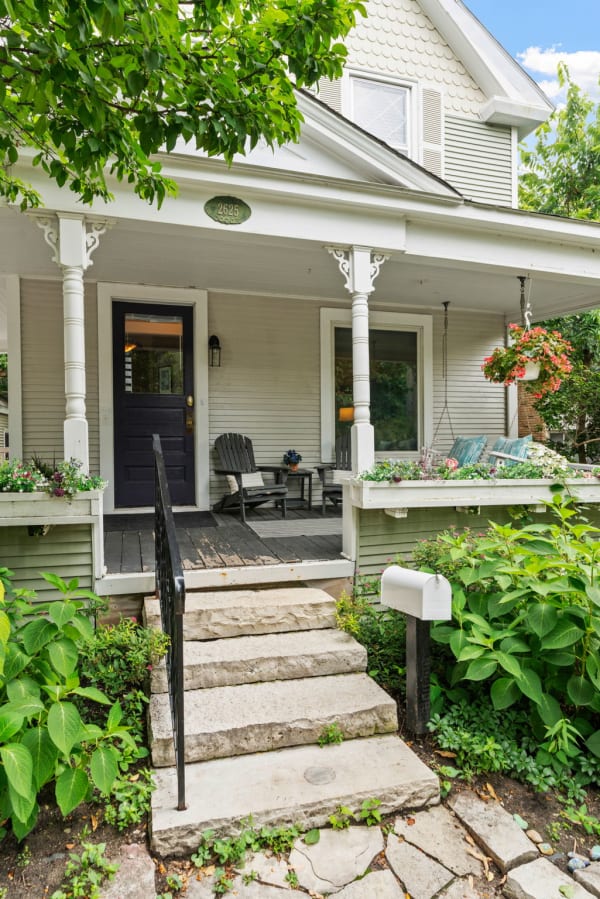 A front porch of a house featuring stone steps, flower boxes, and adirondack chairs.